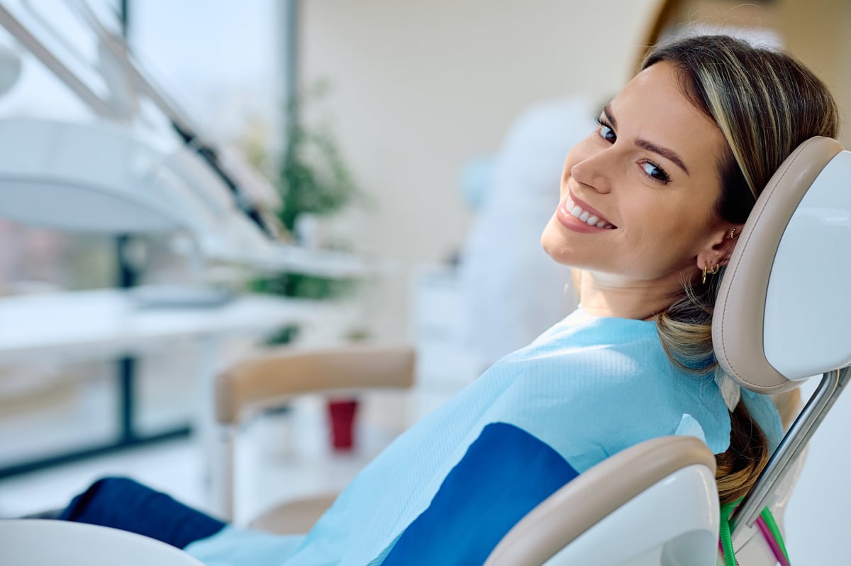 Woman smiling and looking at camera from dental chair, wearing protective bib during dental examination for oral hygiene
