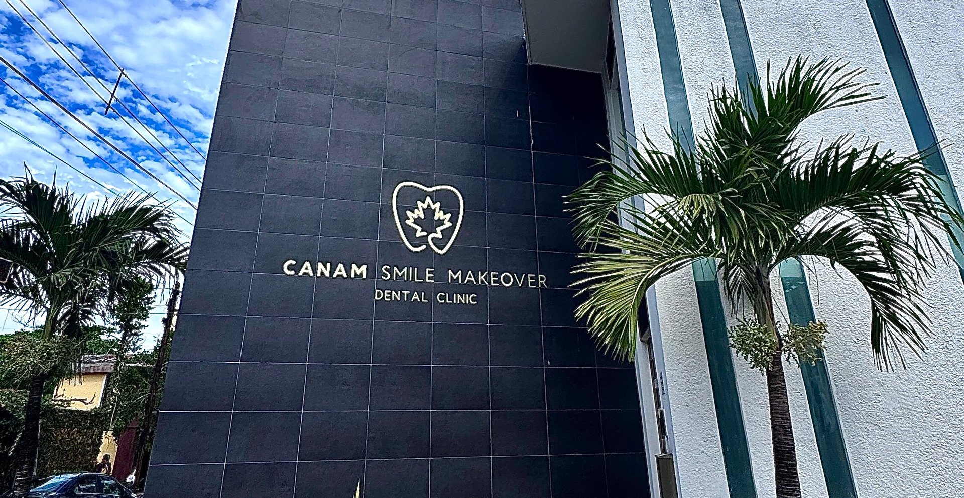 Exterior of CANAM Smile Makeover dental clinic with black facade, logo, and tropical palm trees