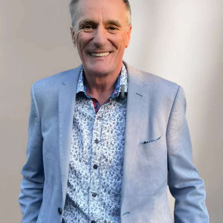 Middle-aged man smiling at camera wearing light blue blazer over blue patterned shirt against neutral background