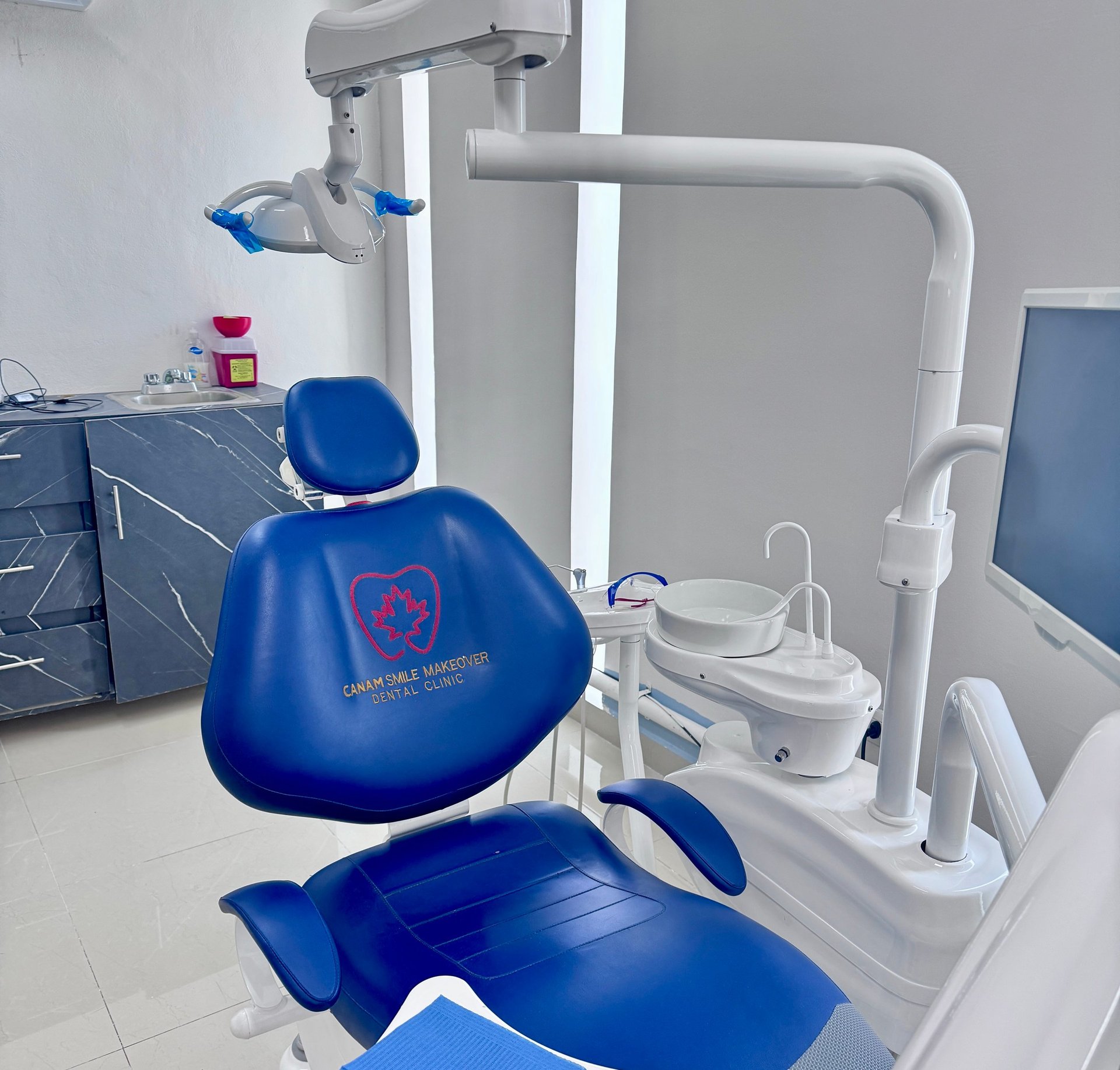 Modern dental office with blue patient chair, overhead lamp, and white suction equipment
