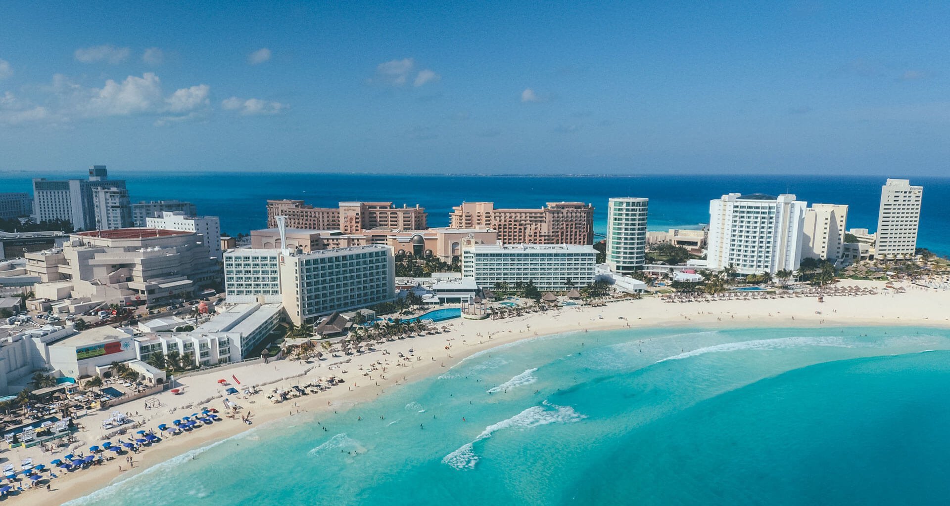 Aerial view of Cancun beach resort with turquoise water, sandy shore, and high-rise hotels along the coastline