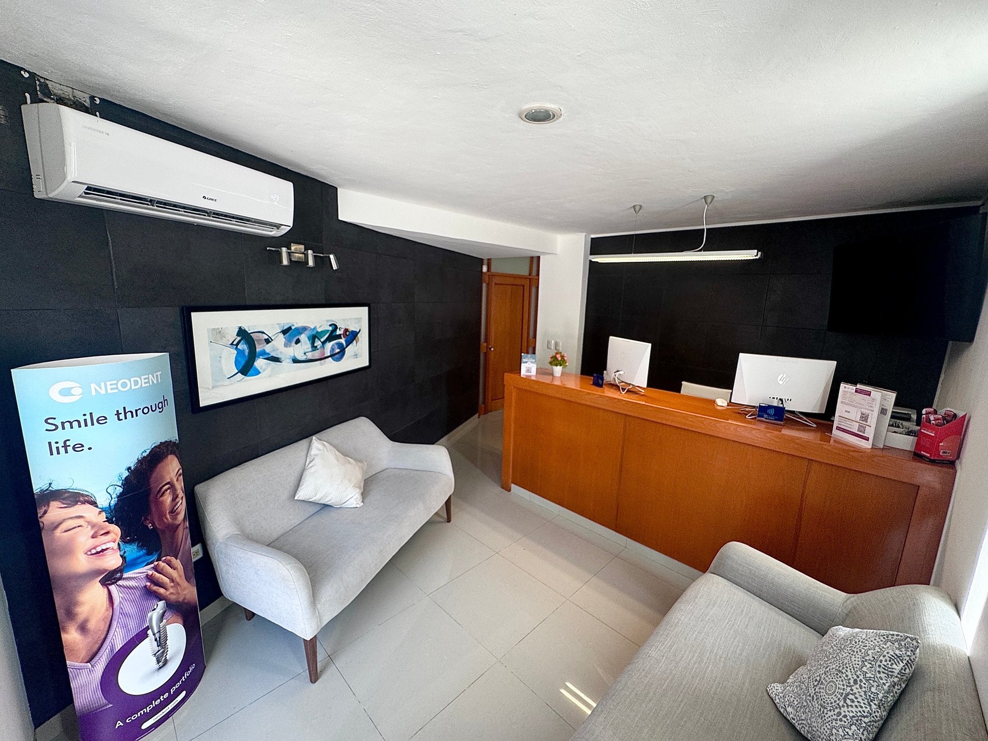 Modern dental office interior with black accent wall, white armchair, wooden reception desk, and digital display screens advertising orthodontic services