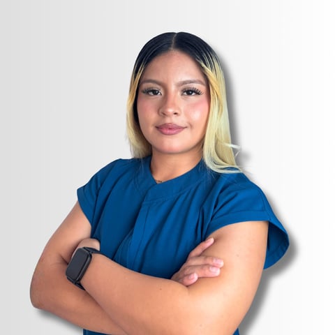 Portrait of a woman with blonde and dark hair wearing a blue t-shirt, arms crossed, against a white background