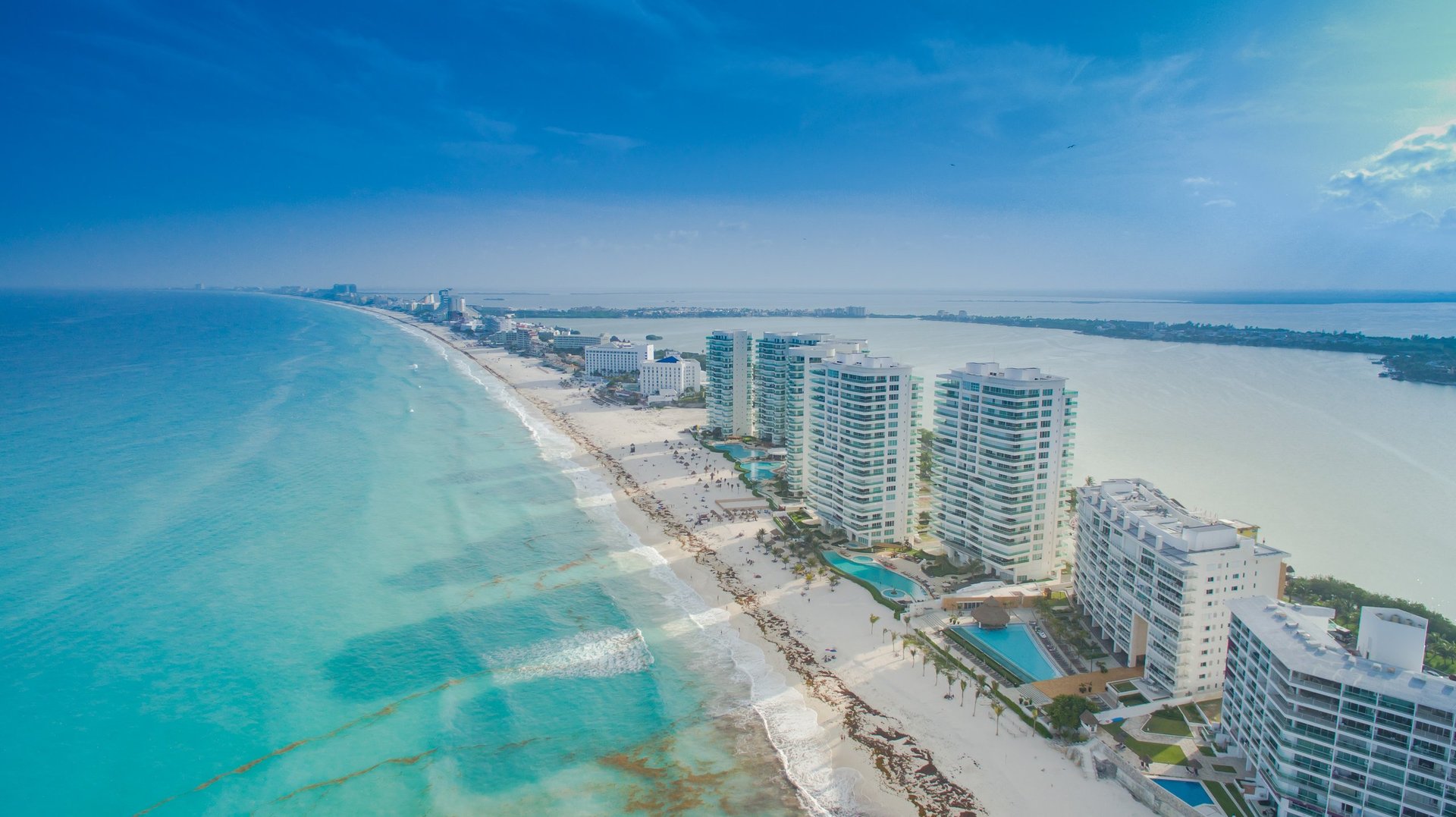 Aerial view of a tropical coastal beach resort with turquoise waters, white sand, and high-rise hotel buildings