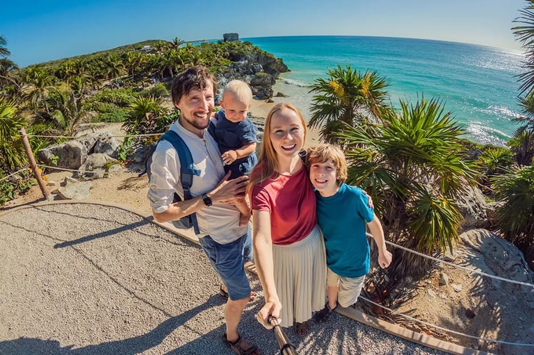 Family of four taking a selfie on a tropical beach overlook with turquoise ocean water and palm trees in background